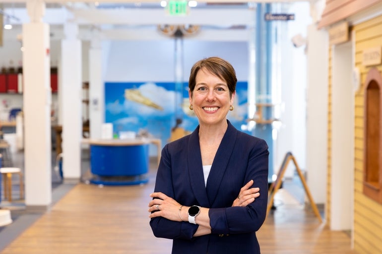 A woman in a blue jacket and white shirt stands in a museum.