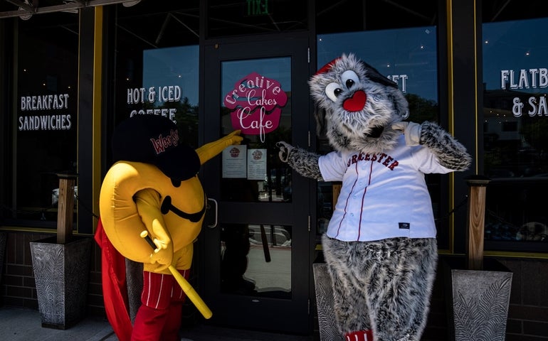 A dog and smiley face mascot gesture outside of a store: Creative Cakes Cafe.
