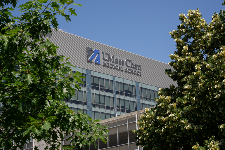 A building with a sign that reads "UMass Chan Medical School" behind two trees