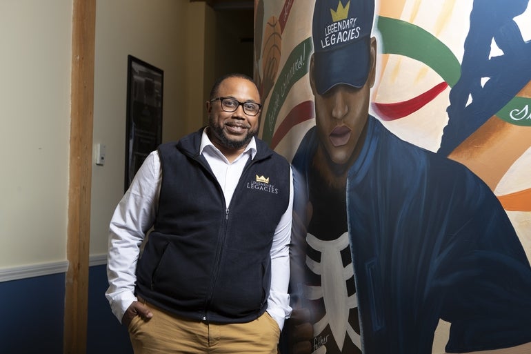 A man stands in front of a mural at his offices.