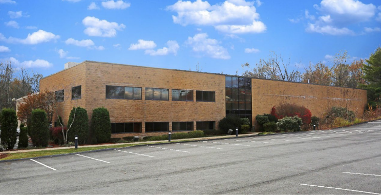 A large brown two-story office building sits in front of an empty parking lot