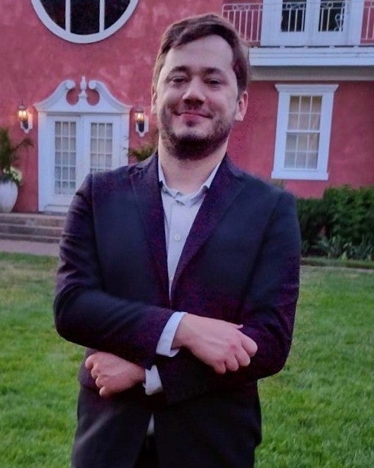 A man in a suit standing on a lawn in front of  a building