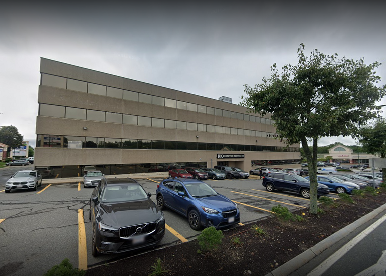 A large grey office building with a parking lot and cars in front. 