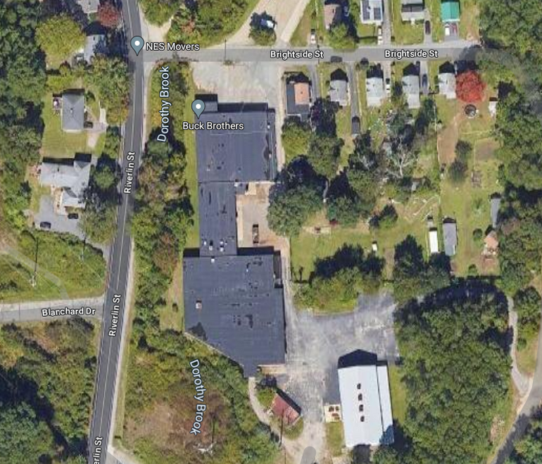 a screenshot of a satelitte image, showing a black-roofed building and smaller buildings around it.