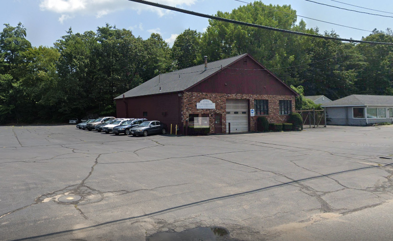 A red brick building with a garage door in front and cars parked alongside. 