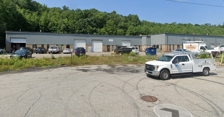 A grey industrial building sits behind a cul-de-sac with a truck parked in it. 