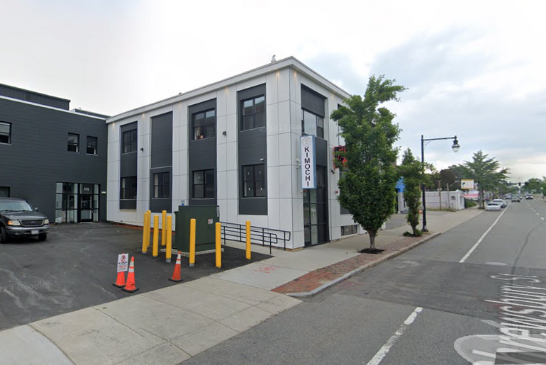 A two story building with a small parking lot alongside it. 