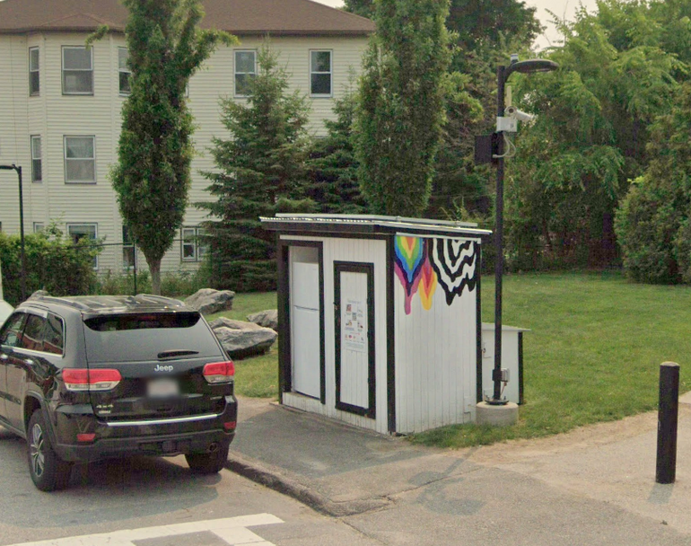 A wooden box with a refrigerator sits next to a sidewalk