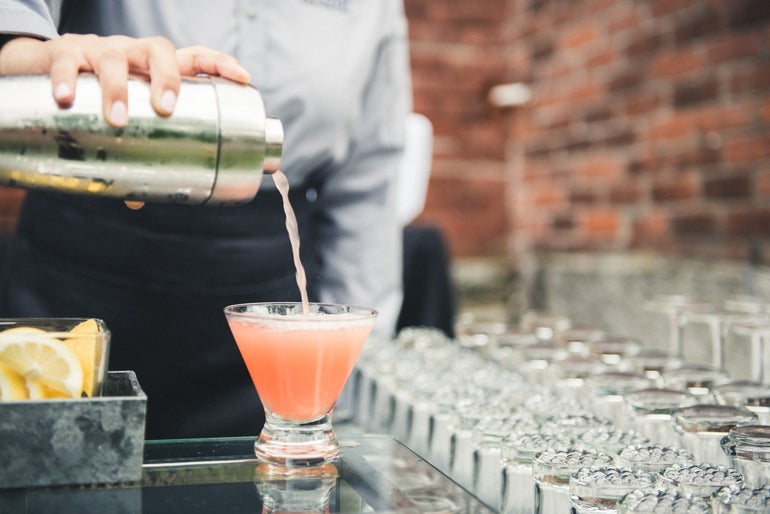 A bartender pours a pink drink from a shaker into a glass cup.