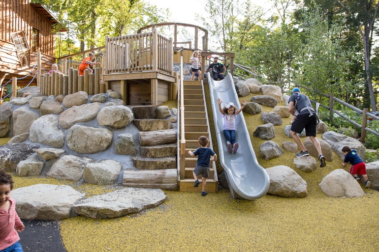 Children and adults play on a rocky playscape.