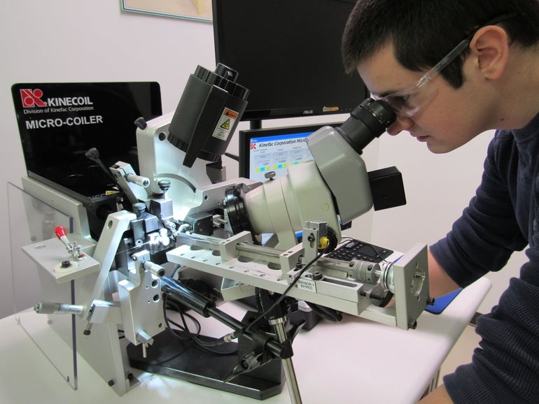 A man wearing safety glasses looks into a manufacturing machine.