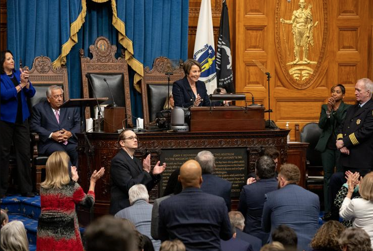 A woman stands behind a podium as a crowd applauds in front of her