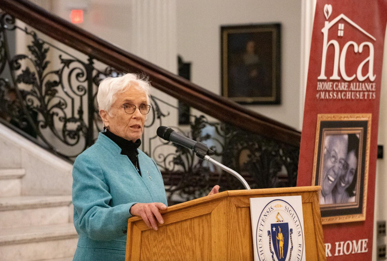 A woman in a blue jacket speaks at a podium