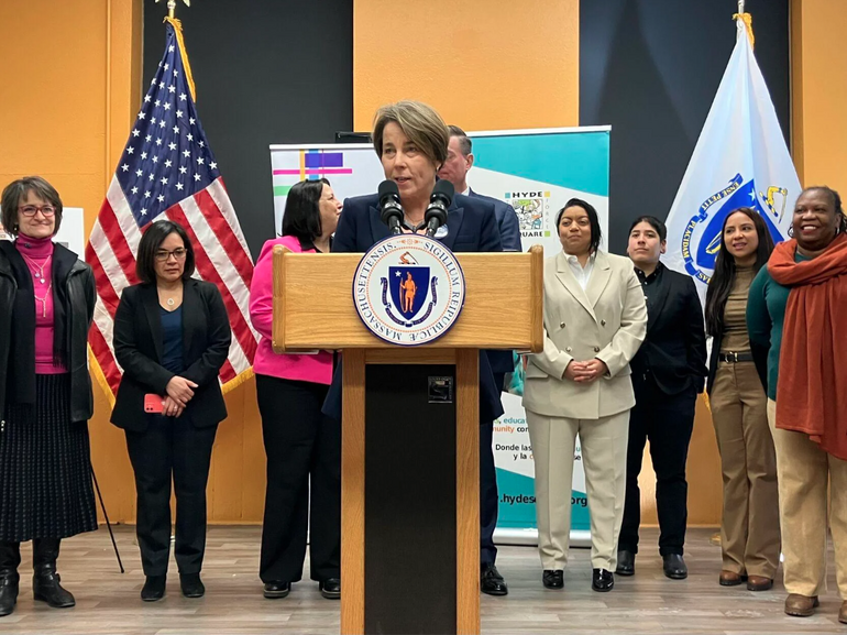 A woman stands at a podium, flanked by a number of people