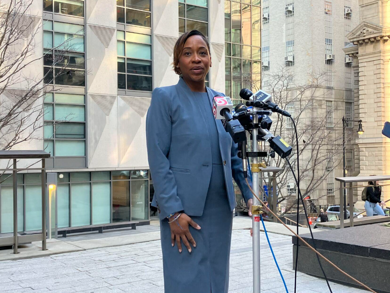 A woman in a suit stands at a podium outside