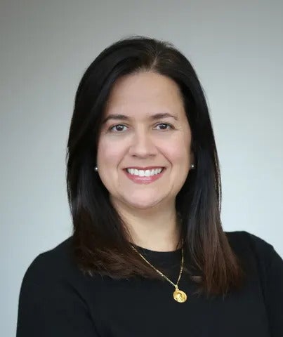 A woman with black hair wears a black shirt and gold necklace