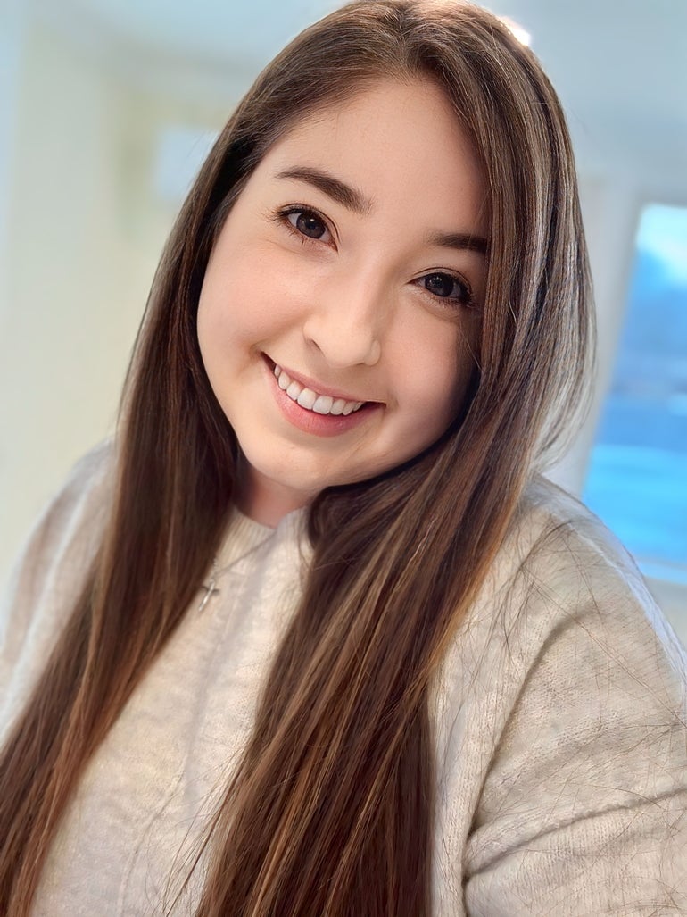 A woman with brown hair wearing a white top smiles at the camera.