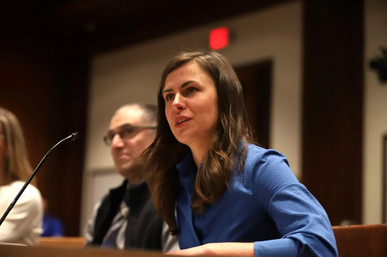 A woman in a blue suit speaks at a microphone during a hearing