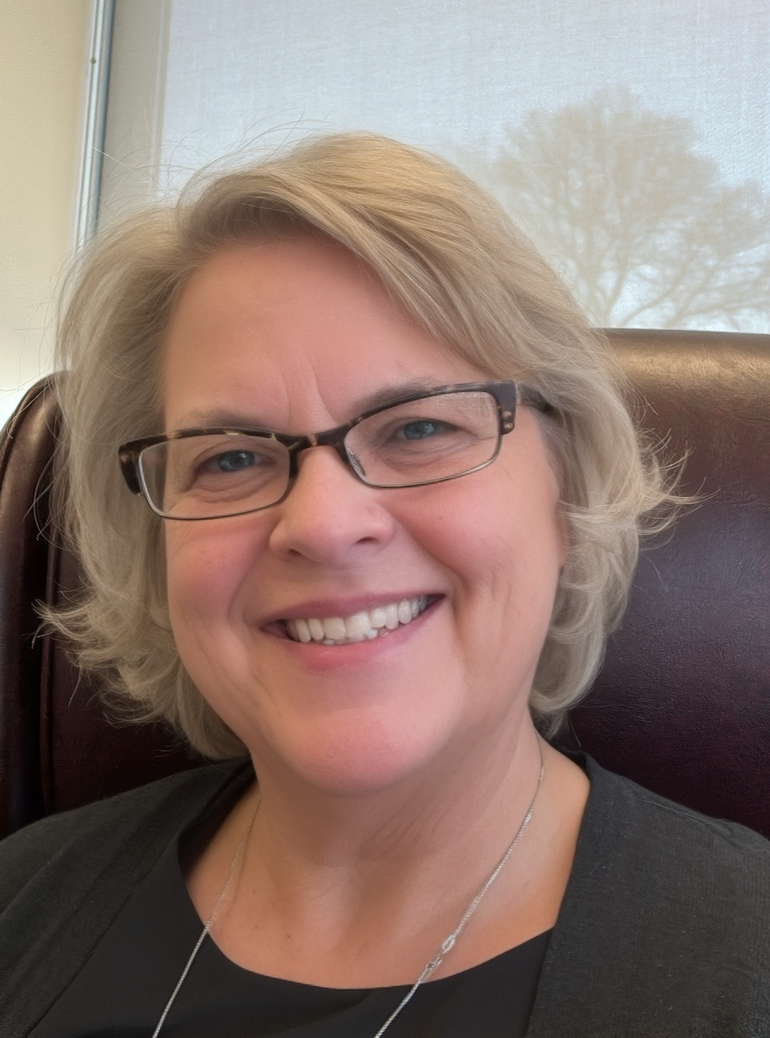 A woman with light, short hair, glasses, and a black shirt smiles for the camera.