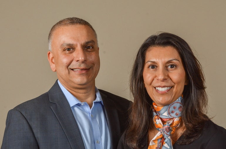 A man wearing a suit and a woman wearing a scarf smile at the camera.