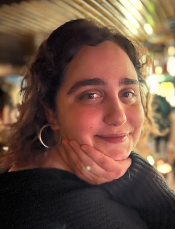 A woman with curly hair wears a black sweater and big hoop earrings.