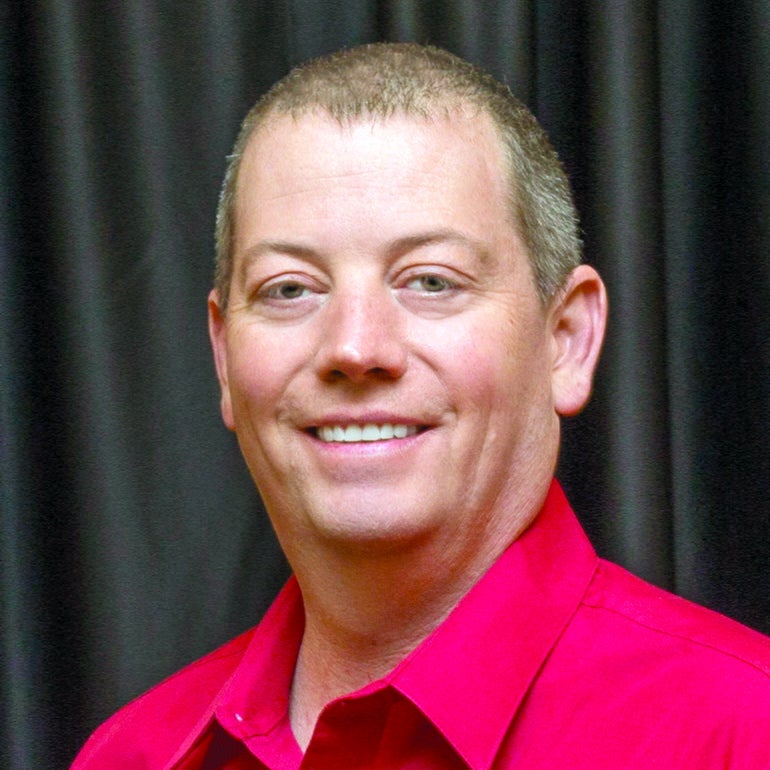 A man in a red shirt smiles for the camera.