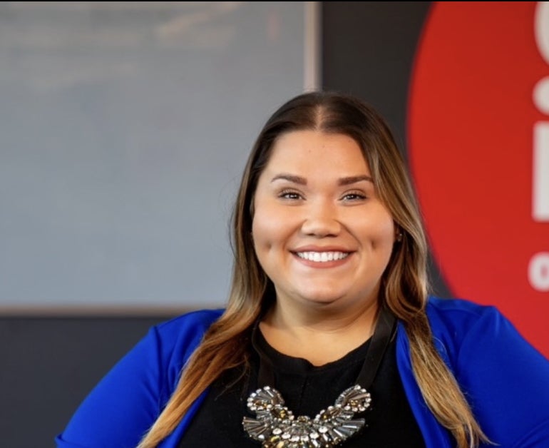 A woman with long hair wears a black shirt and a blue jacket