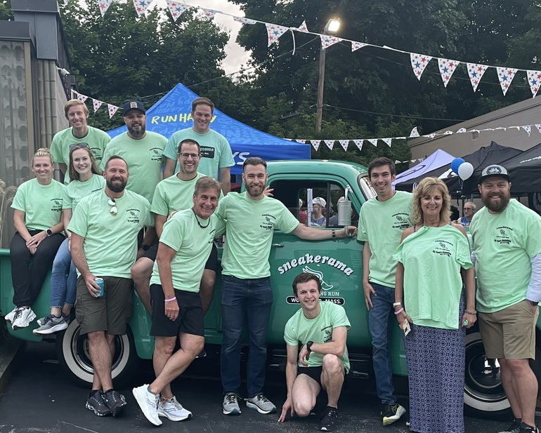 A group of men and women in light green shirts sitting on and standing in front of a green truck.