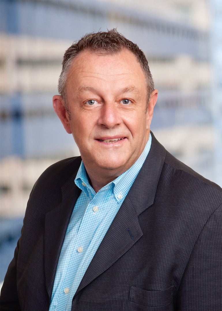 A man wearing a blue shirt and jacket smiles at the camera.