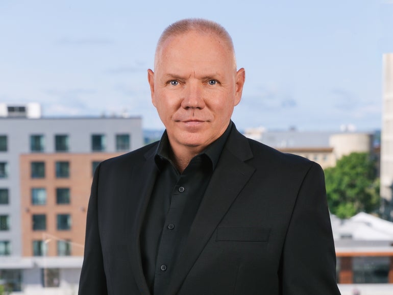 A man in a black suit with Worcester's skyline behind him