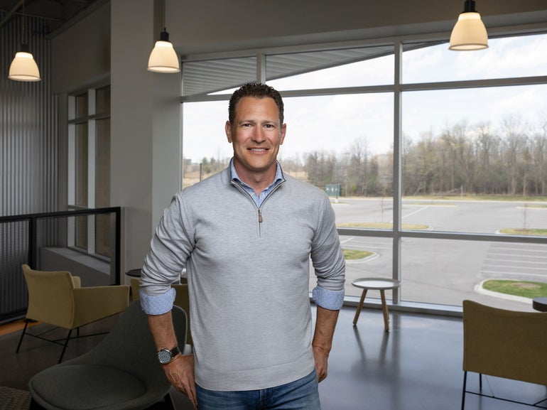 A man in a zip-up grey sweater stands in a modern office