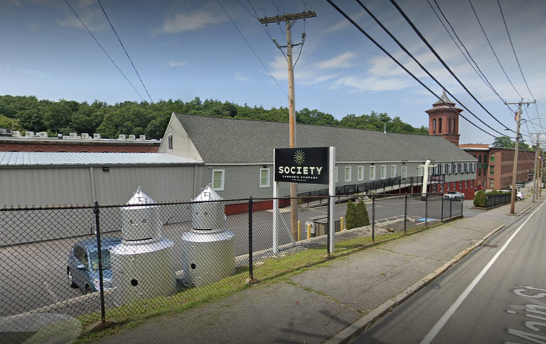 A one-story commerical building sits behind a fence and a parking lot.