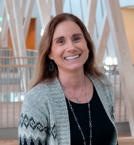 A woman with long light brown hair, a black shirt, and grey cardigan. 