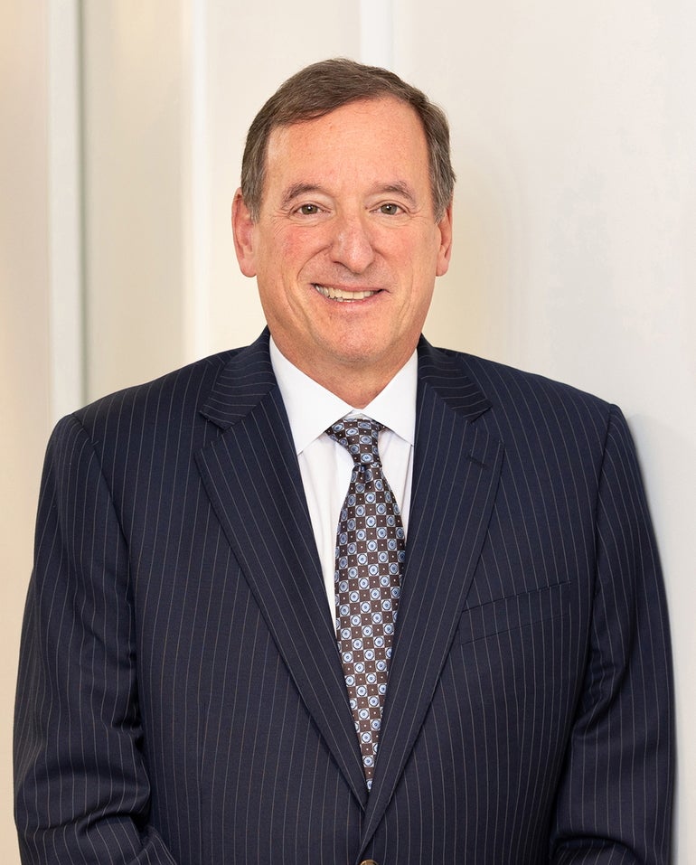 A headshot of man in a pinstripe suit and patterned tie 