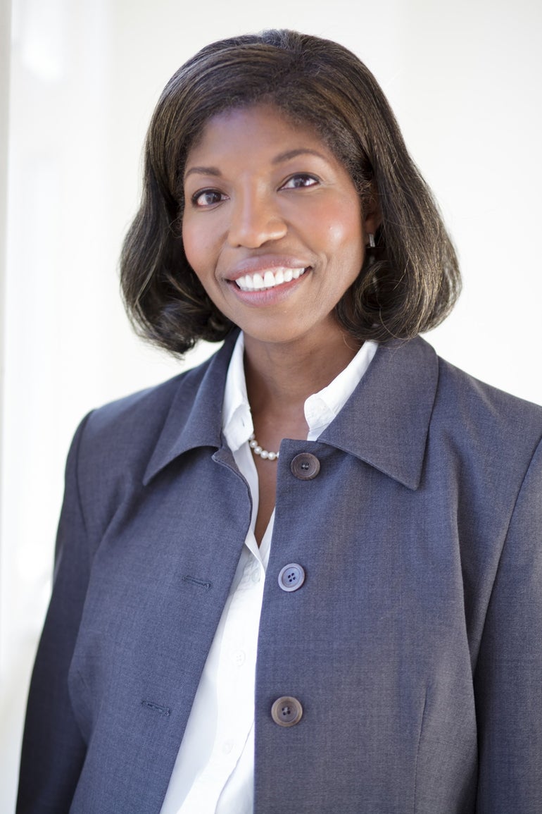 A woman in a blue jacket and white button down with a pearl necklace smiles for the camera.