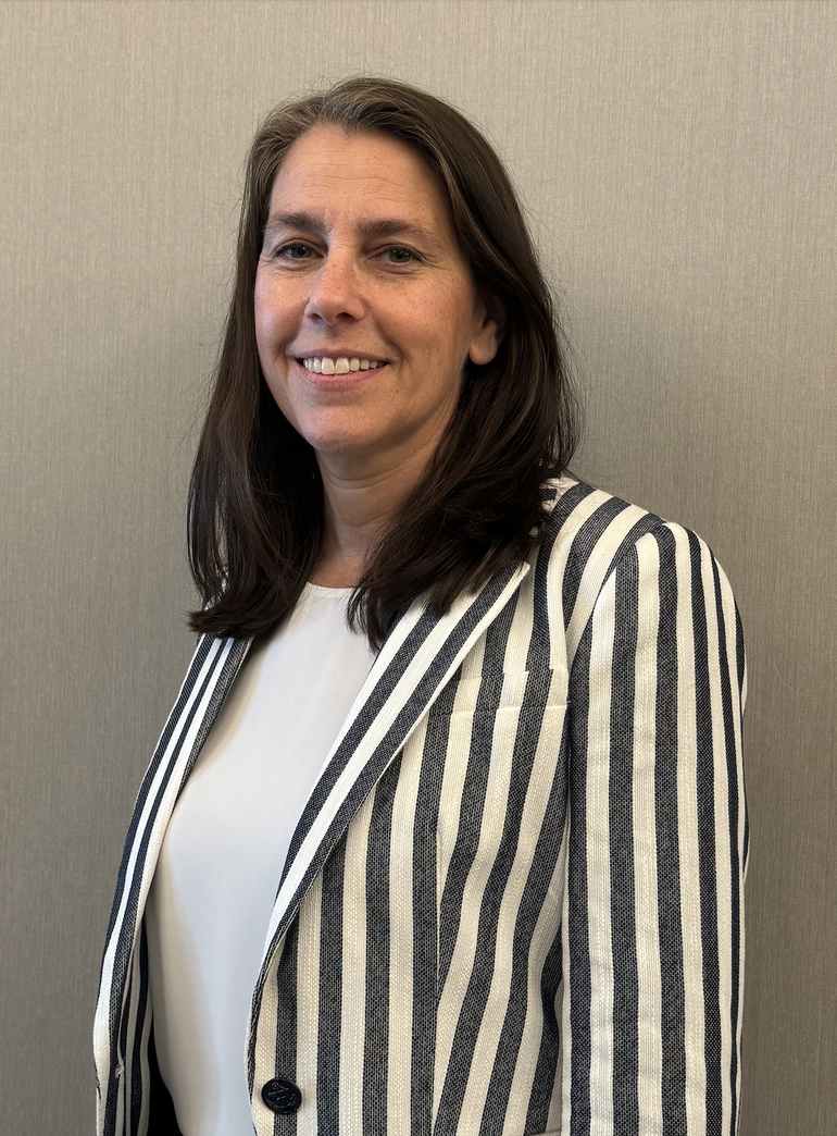 A woman with shoulder length brown hair and a grey and white pinstripe jacket.