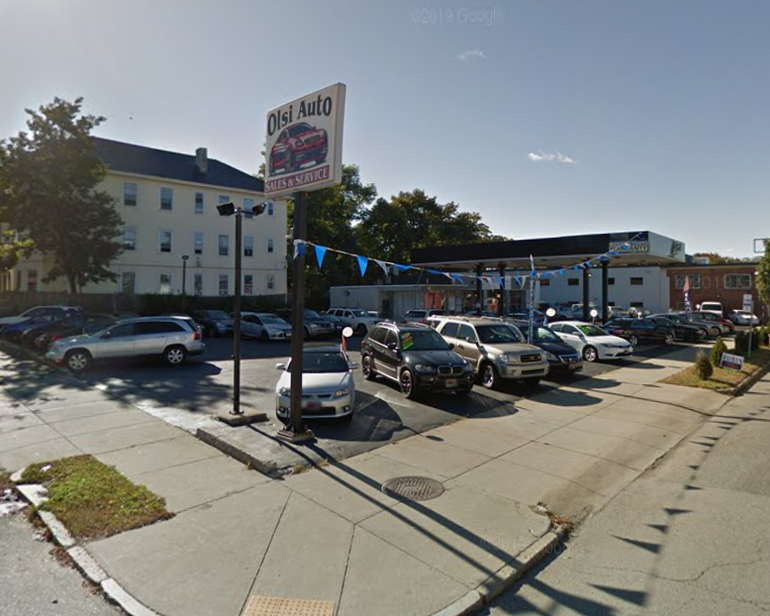 a used car lot featuring a gas pump, lots of cars, and a sign