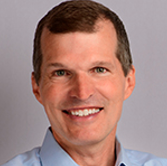 A man with short dark hair and a light blue shirt smiles for the camera