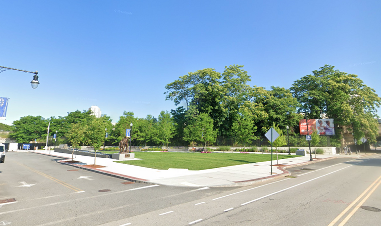 A small grass-filled plaza featuring a statue and trees