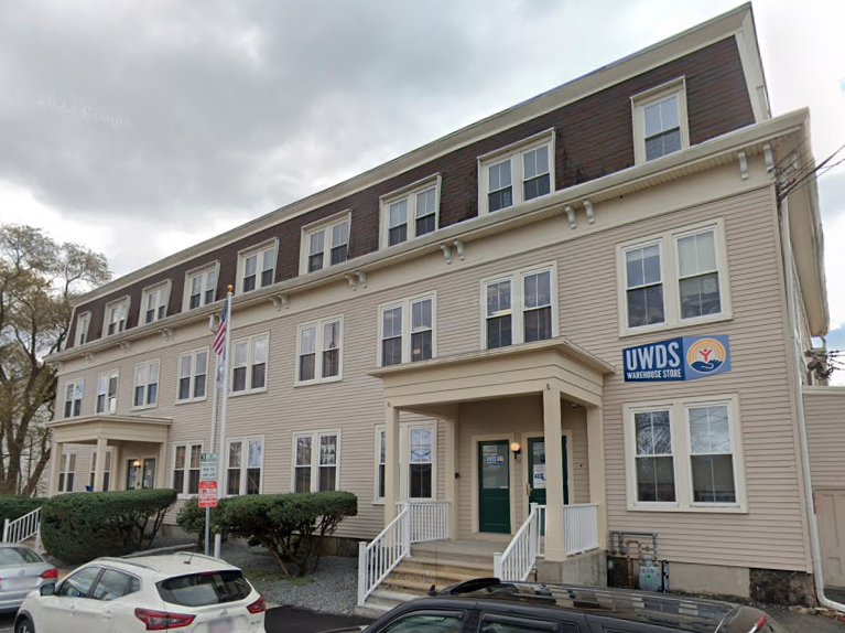 A beige building with a grey top and two entrances with steps leading up to them with an American flag between.
