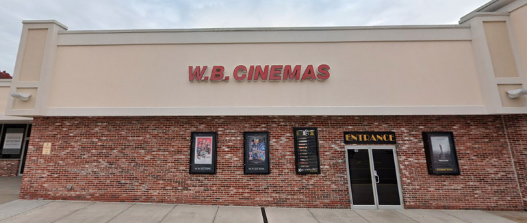A brick building with a light peach top with movie posters displayed and an enterance sign above two doors.