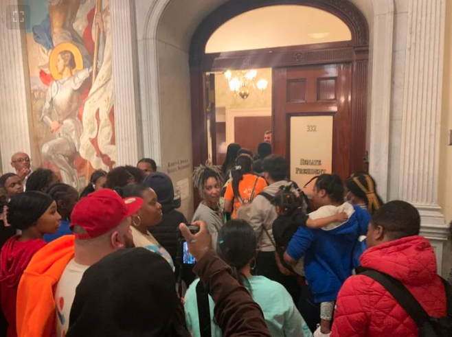 A group of people filter through a lobby and through large wooden doors.