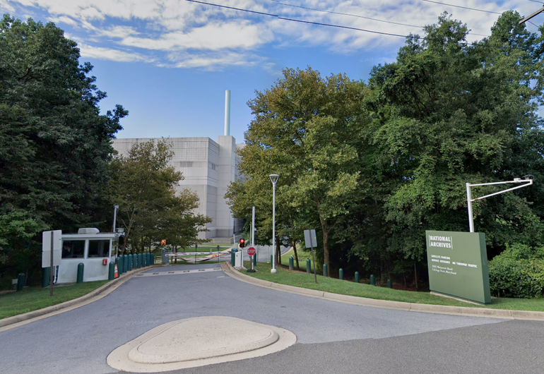 The entrance to a government site, with a guard post and gate in front of a large concrete building