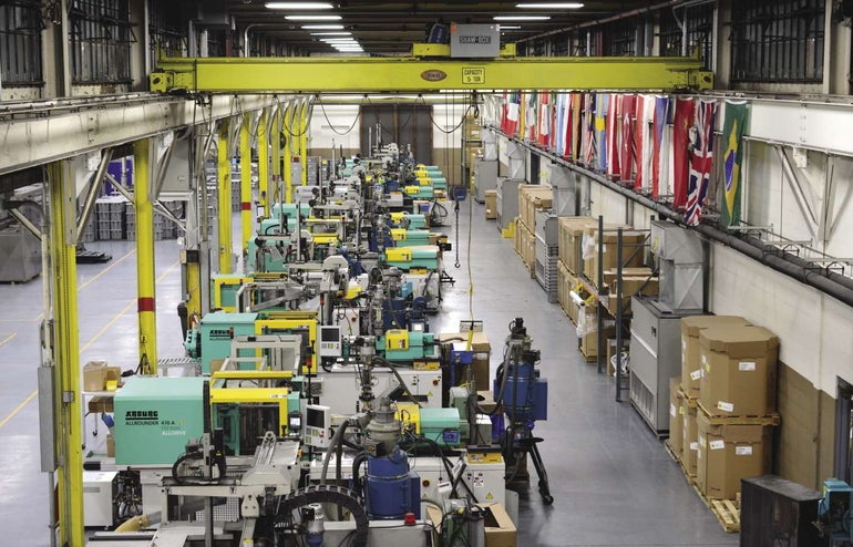 Inside a factory with yellow beams, green, yellow, and white machines, and flags lining the upper right hand wall.