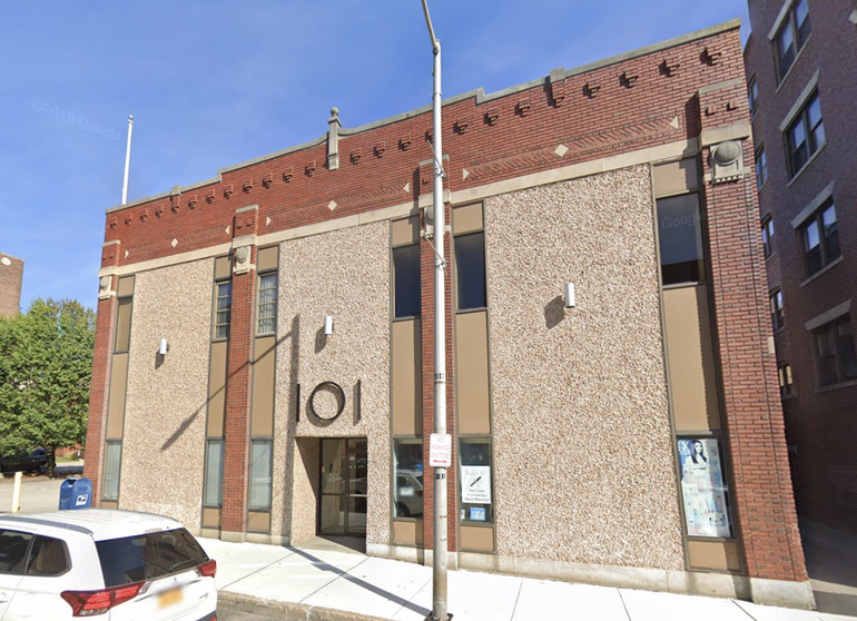 A brick building with a "101" sign above the entrance sits behind a sidewalk.