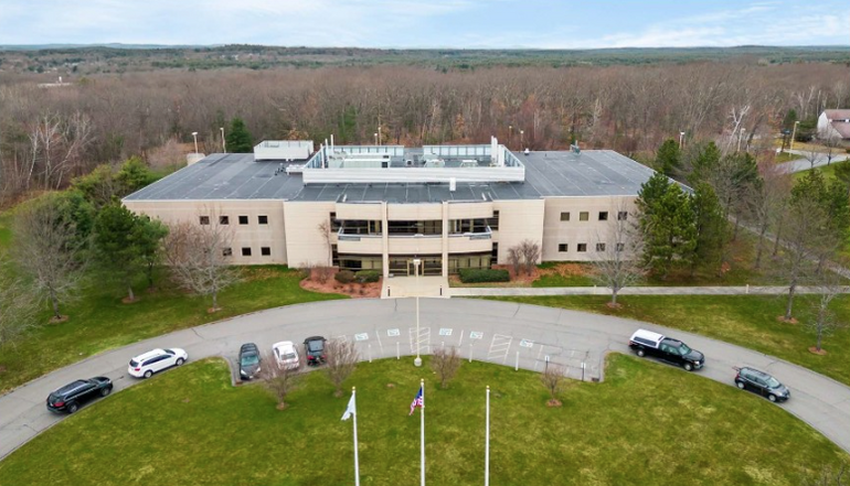 A manufacturing building with a semi-circle road in front and a forest behind it