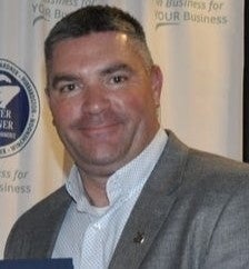 A man wears a grey suit jacket and light blue button down.