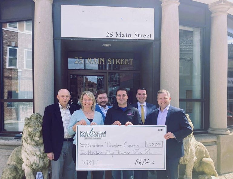 A group of people with an oversized check in front of a commercial property.
