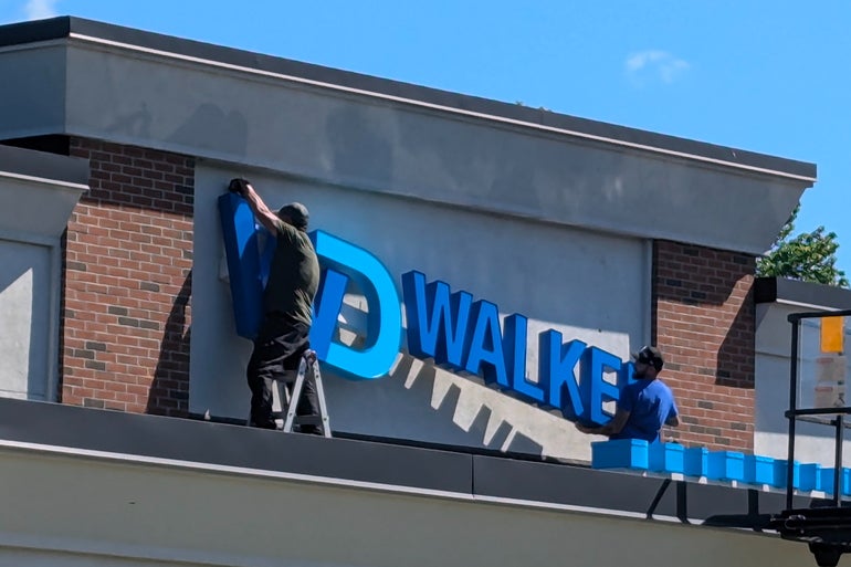 Workers hang a large sign on a building's roof
