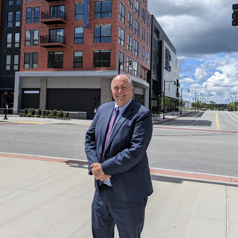 man in a suit stands across a street from a mixed-use apartment building